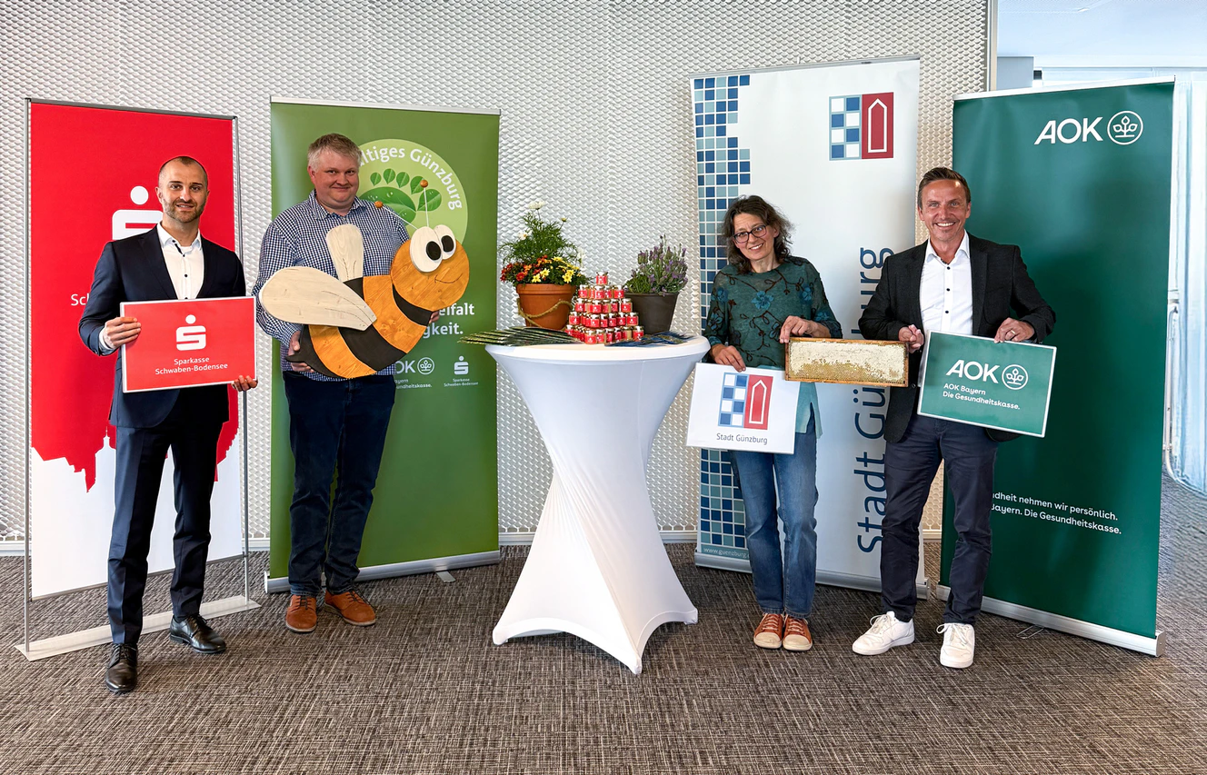Die Bienenpaten Andreas Steinbacher, Mitglied des Vorstands der Sparkasse Schwaben-Bodensee, Christine Hengeler, Umweltfachkraft der Stadt Günzburg, und Bernd Mayer, Direktor der AOK Günzburg, heißen die Bienen von Imker Wolfgang Heininger, Vorsitzender des Imker-Kreisverbandes Günzburg, symbolisch mit einer großen Holzbiene für die Blühflächen in der Stadt Günzburg herzlich willkommen. — © Demet Karatas/Sparkasse Schwaben-Bodensee