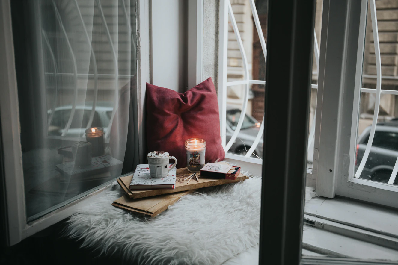 Ein gemütliches Fensterbrett auf dem ein Kissen, eine Kerze und eine Tasse heiße Schokolade stehen