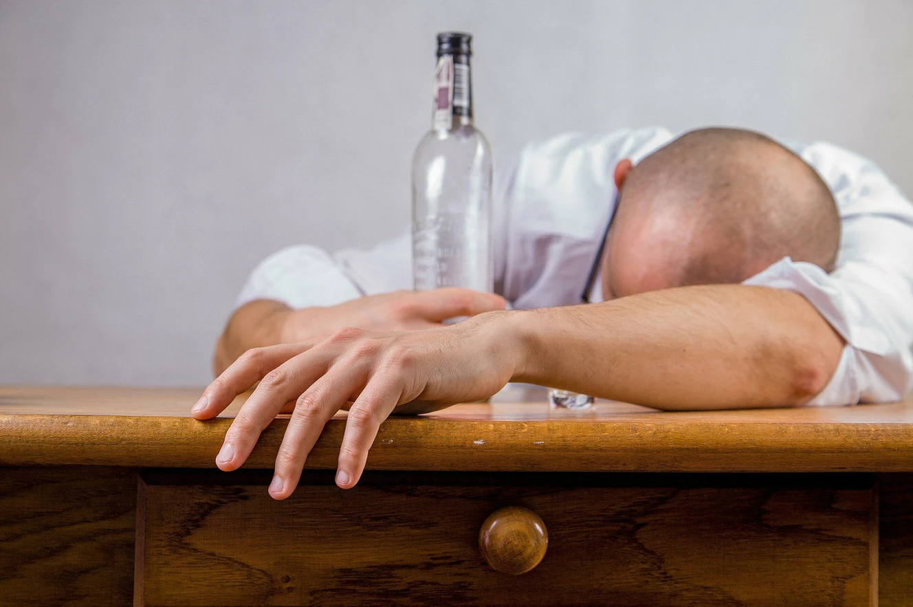 Ein Mann liegt mit dem Kopf auf einem Tisch und hat eine Flasche Alkohol neben sich stehen