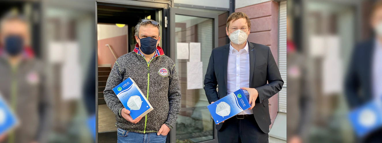 Landrat Hans Reichhart, wie er Masken an den Geschäftsführer der Caritas, Mathias Abel, übergibt  — © LRA Günzburg, Schack