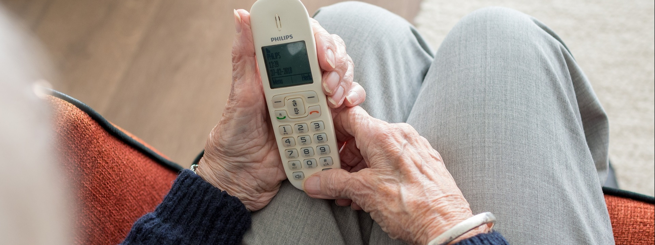 Eine alte Frau hält ein Festnetztelefon in der Hand
