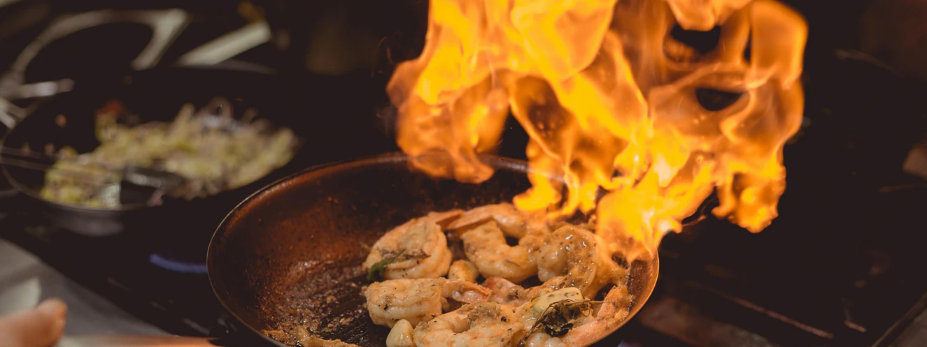 Eine Portion Shrimps wird unter offenem Feuer in einer Bratpfanne angebraten