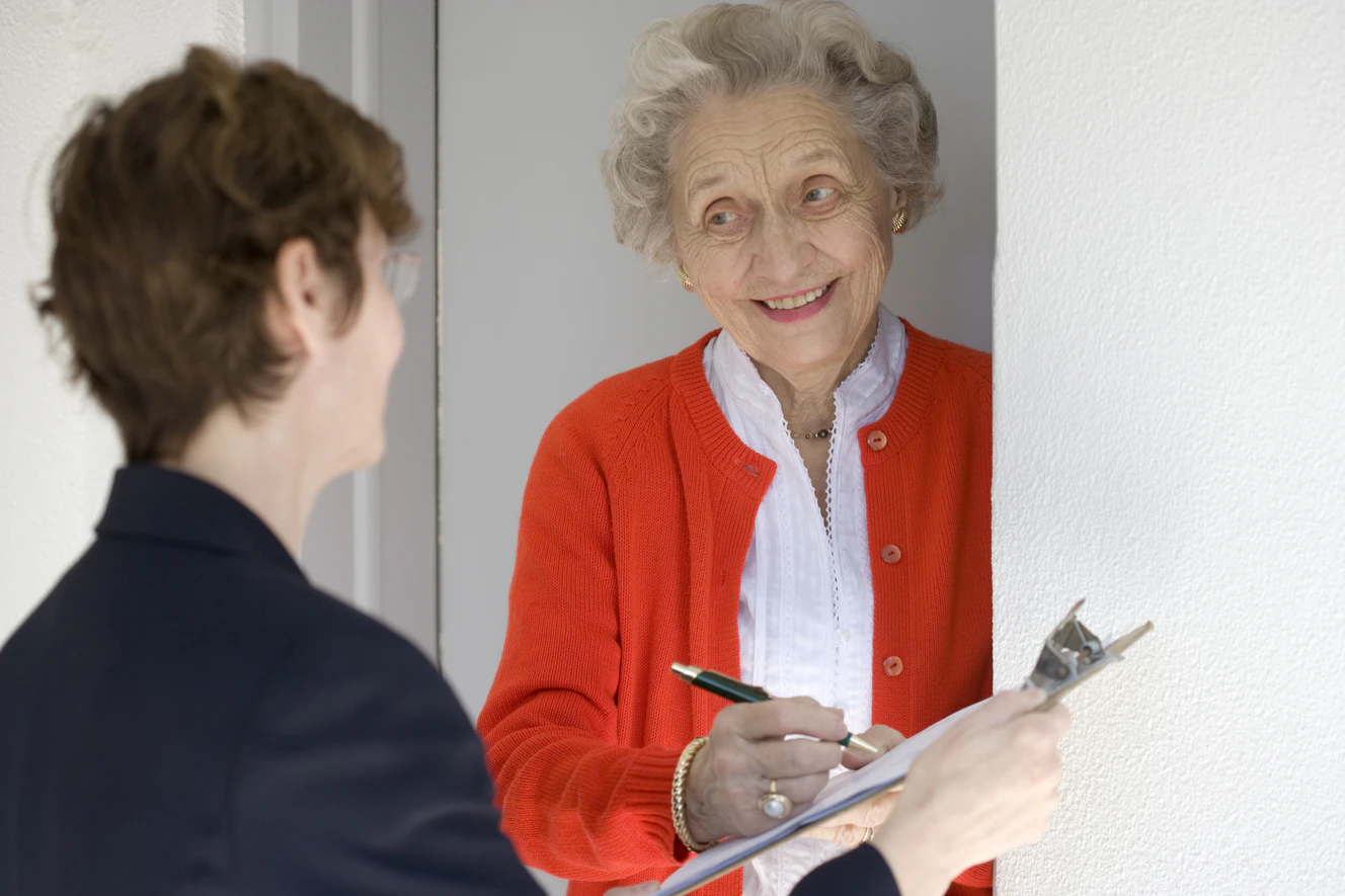 Eine alte Frau unterschreibt an der Haustür einen Vertrag