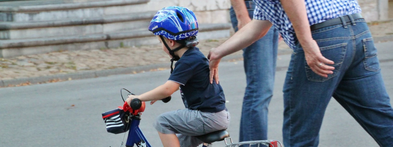 Ein Kind mit Fahrradhelm bekommt von seinen Eltern das Radfahren beigebracht