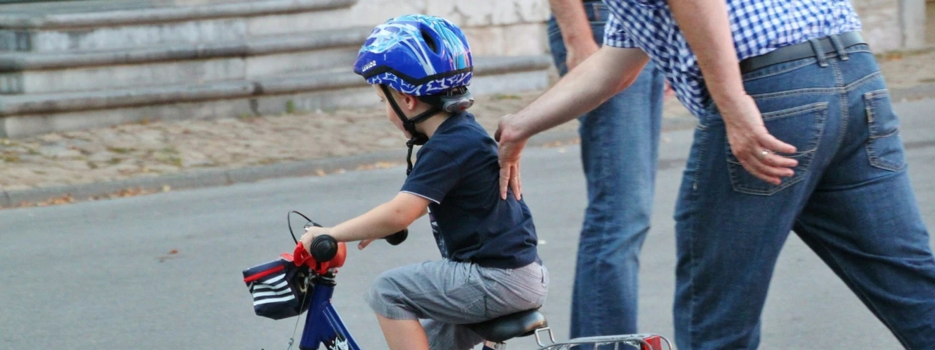 Ein Kind mit Fahrradhelm bekommt von seinen Eltern das Radfahren beigebracht
