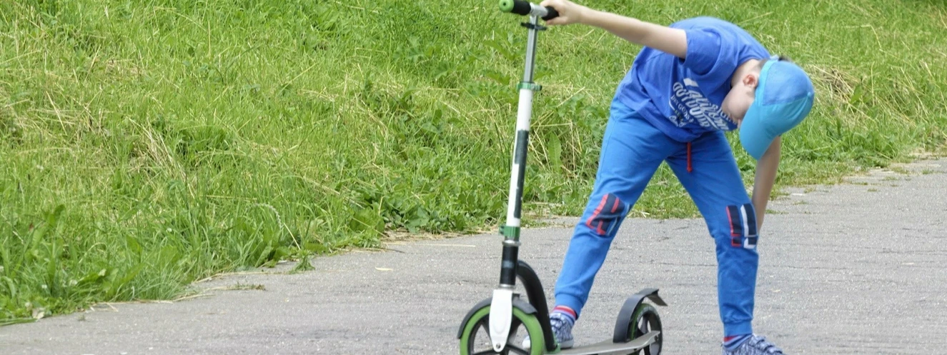 Junge begutachtet seinen Tretroller auf der Straße