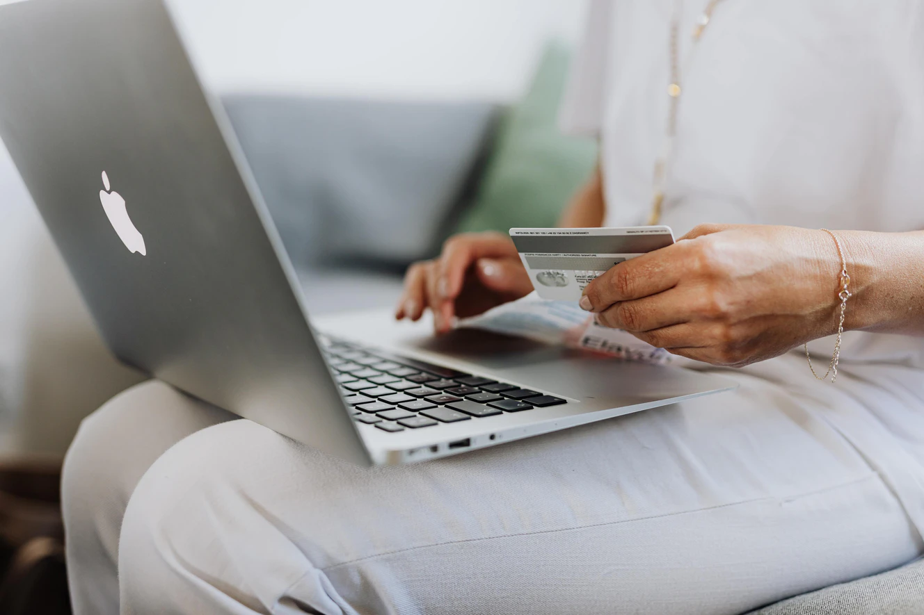 Person sitzt mit Kreditkarte in der Hand am Laptop