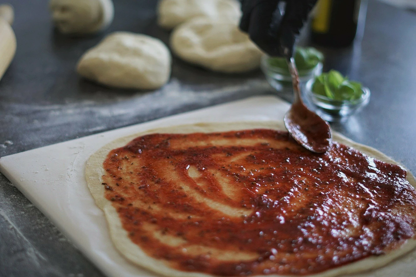 Pizzateig wird mit Tomatensauce bestrichen