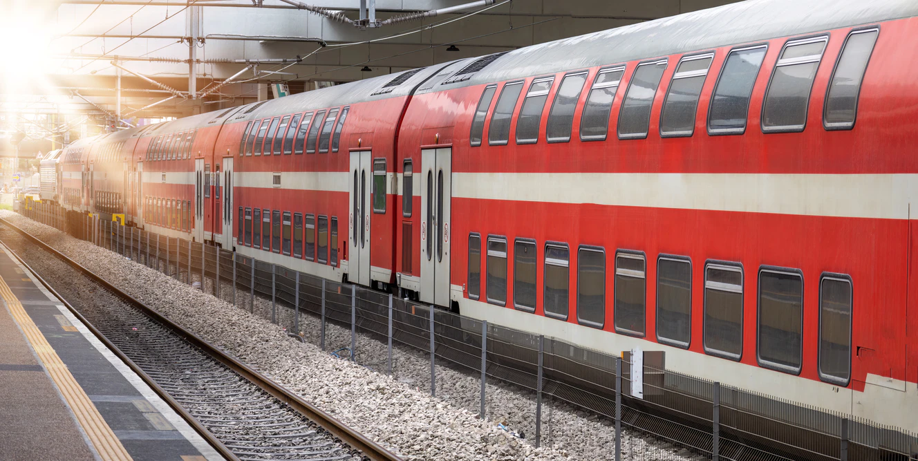 Zug fährt aus einem Bahnhof bei Sonnenschein.