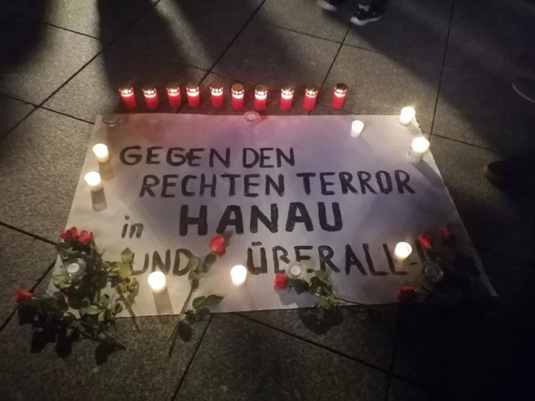 Kerzen und Blumen auf einem Banner mit der Aufschrift "Gegen den rechten Terror in Hanau und überall"